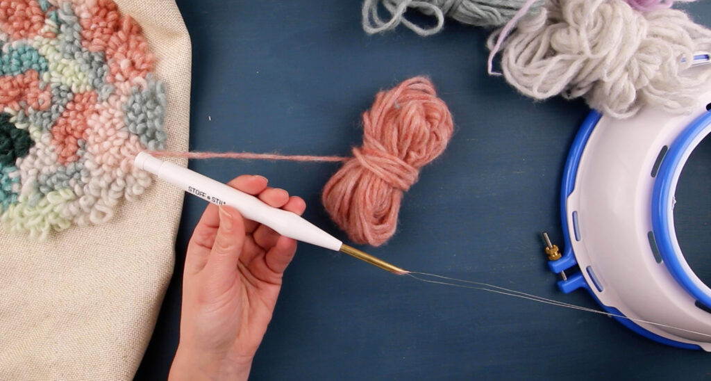 Hånd som trekker tråden gjennom Munch needle, og trer den så den er klar for bruk.